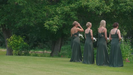 bridesmaids in dark green dresses waiting for first look bride dress in garden