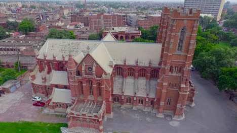 A-beautiful-old-Church-aerial-view,-A-black-kite-sat-at-the-Cross-of-the-Church,-The-Church-with-red-bricks-and-two-cars-parked-at-the-corner