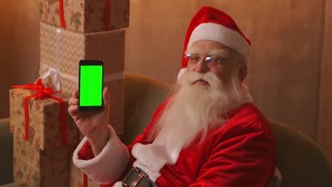 Santa-Señala-Con-El-Dedo-La-Pantalla-Verde-Del-Teléfono-Móvil.-Venta-De-Navidad.-El-Anciano-Papá-Noel-Muestra-Una-Pantalla-Con-Un-Cromakey.-Imágenes-4k-De-Alta-Calidad