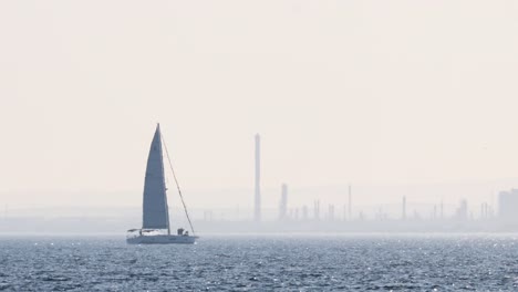 sailboat gliding across ocean with industrial backdrop