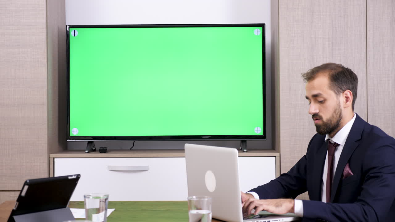 Businessman working in office with green screen TV and laptop