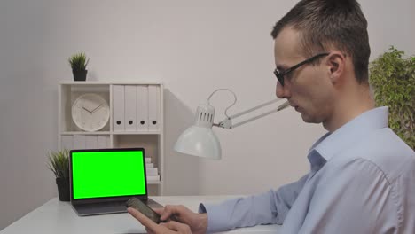 vista trasera del hombre de negocios mira la pantalla verde de la computadora portátil en la oficina