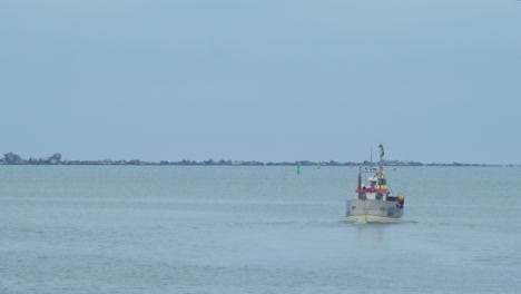 small white coastal fishing boat leaves the port of liepaja, overcast day, fisherman ready to catch a fish in a baltic sea, local business, distant shot