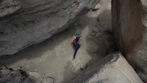 top view of young woman walking on hiking trail in narrow slot canyon between rocks on sunny day