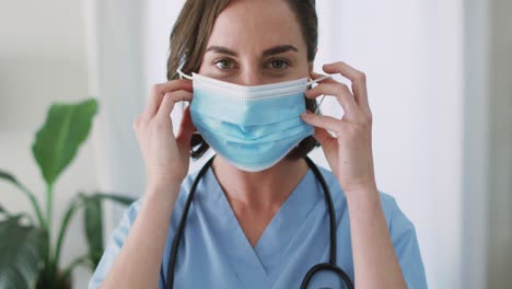 Portrait-of-caucasian-female-doctor-wearing-face-mask-at-home