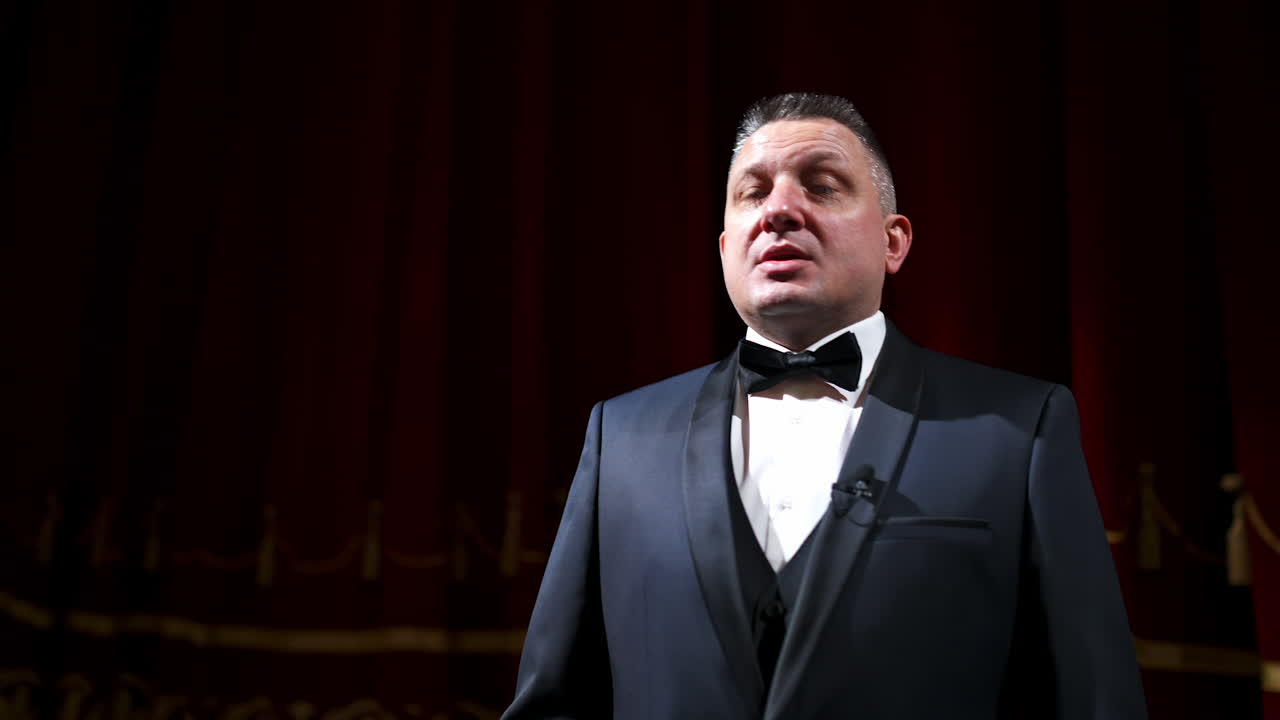 Man is speaking in the light of the floodlights standing on stage to the camera. Actor, artist on performance. Activ gestures with hands.