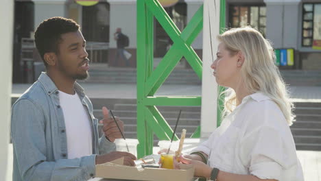 amigos charlando mientras comparten pizza y beben, parados en una mesa al aire libre en la calle