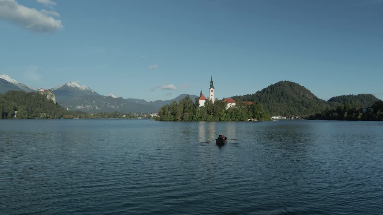Person rudert Boot auf dem Bleder See mit Inselkirche und Burg