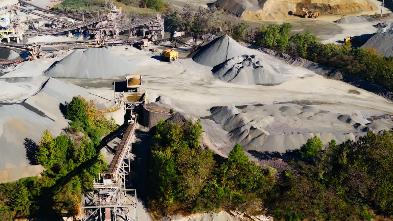 Aerial overview of gravel mounds and processing plant at quarry, dump truck preparing to load conveyor belt