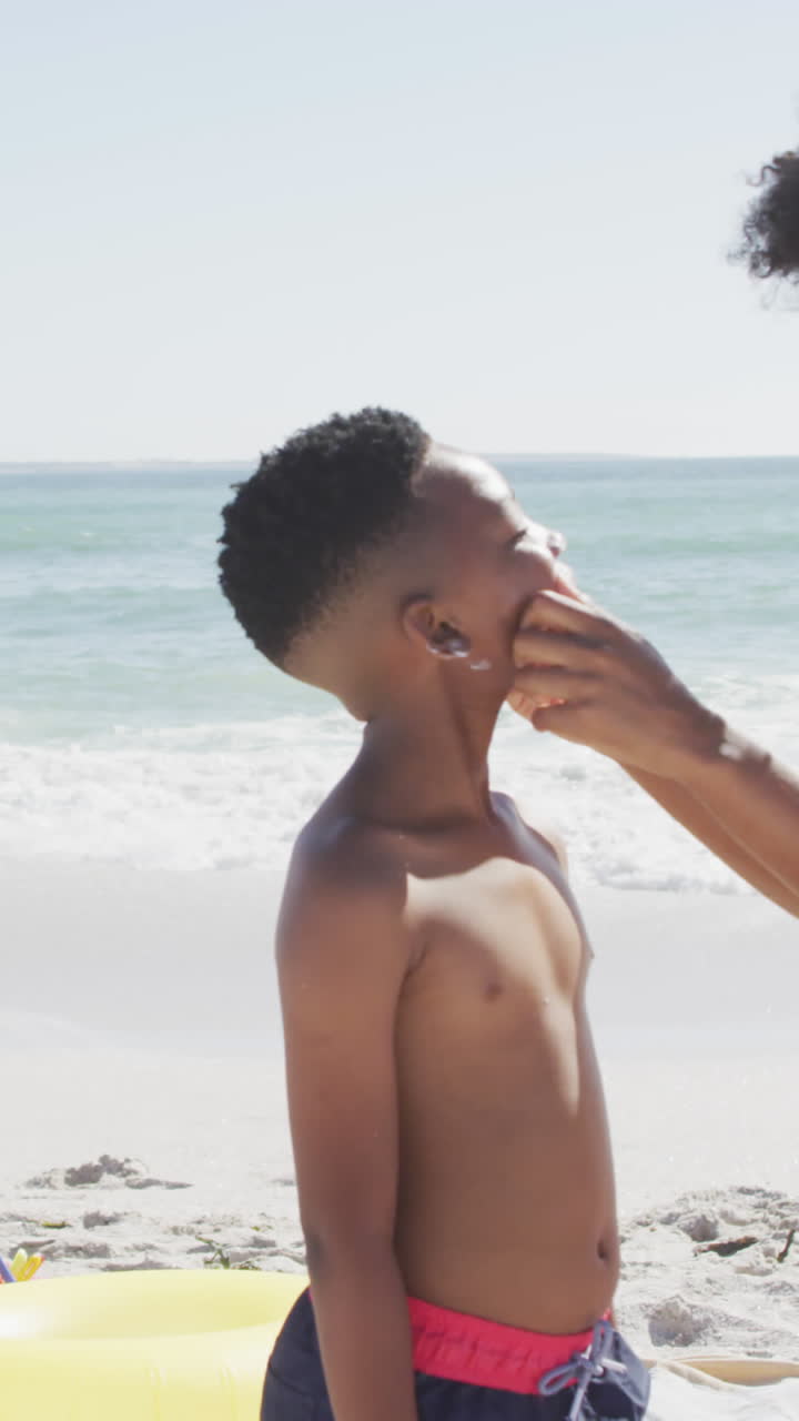Smiling african american family using sun cream on sunny beach