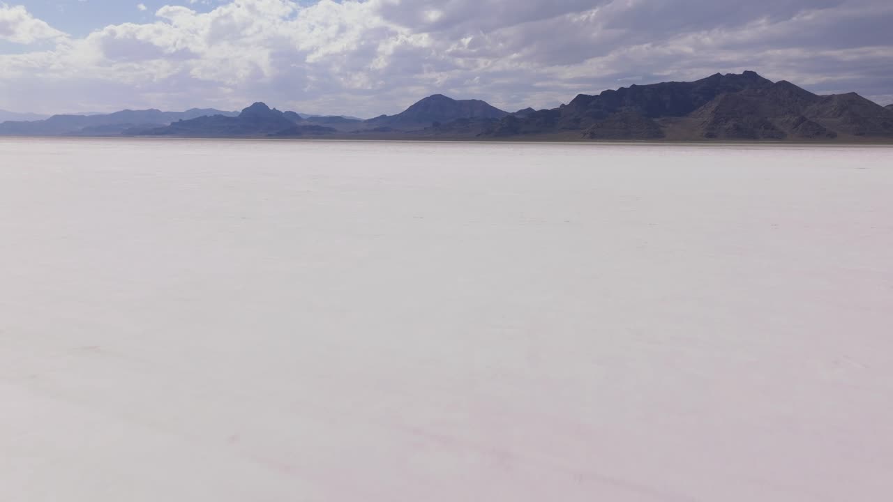 Aerial pullback over serene calm white salt flats landscape with rugged mountains in distance