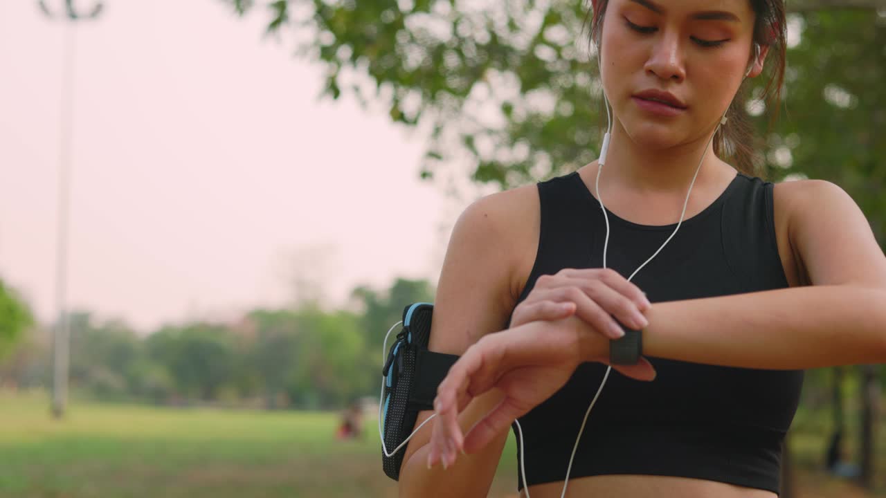 an asian women runner using smart watch to monitor her performance. athlete setting fitness app on smartwatch before running session. women runner in sportswear and earphones Outdoor jogging