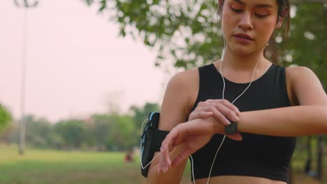 an asian women runner using smart watch to monitor her performance. athlete setting fitness app on smartwatch before running session. women runner in sportswear and earphones outdoor jogging