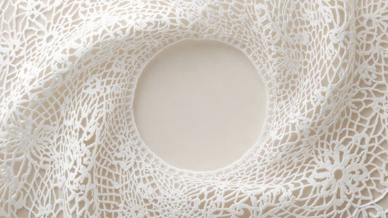 Pulling back camera revealing white lace doily expanding on tan surface, revealing scalloped rim