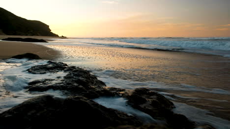 Agua-De-Mar-Fluyendo-De-Regreso-Por-La-Roca-En-La-Playa,-Amanecer-Dorado