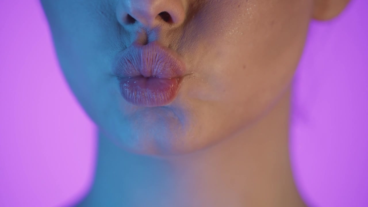 Primo piano della bocca di una donna, labbra in espressione di bacio, scatto in studio colorato