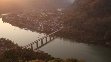 el sol se pone sobre el río con un puente que lo atraviesa en la ciudad montañosa de nong khiaw en laos, sudeste asiático
