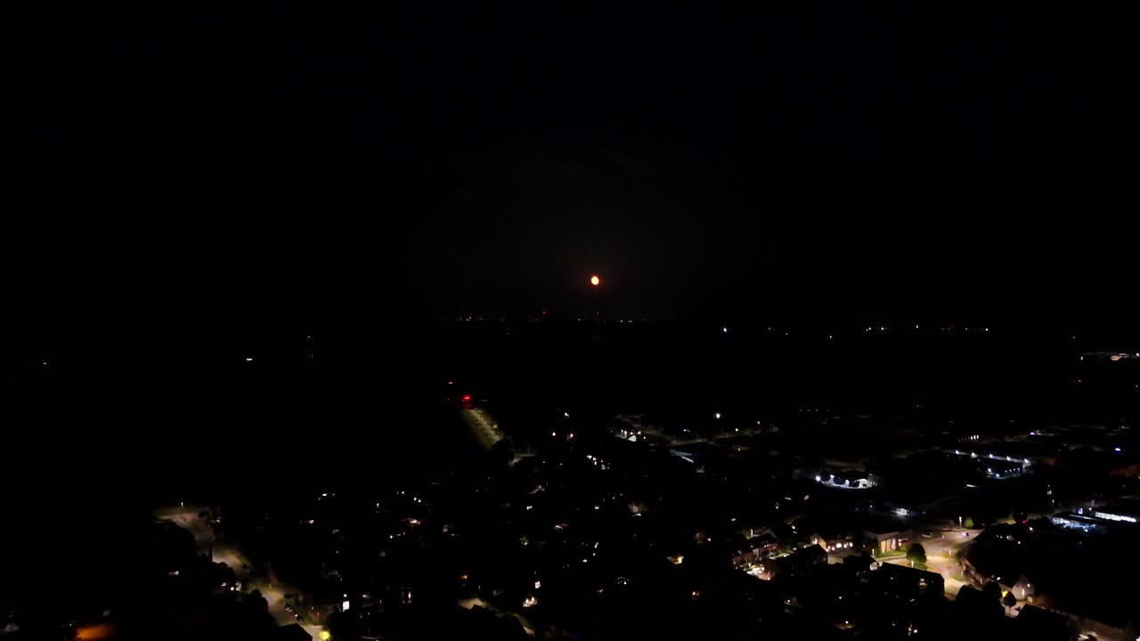 Lighting city in American town at night with orange full moon at sky. Aerial forward wide shot. Cars on street. Quiet Housing area with illuminated lantern in town of USA. Peaceful landscape