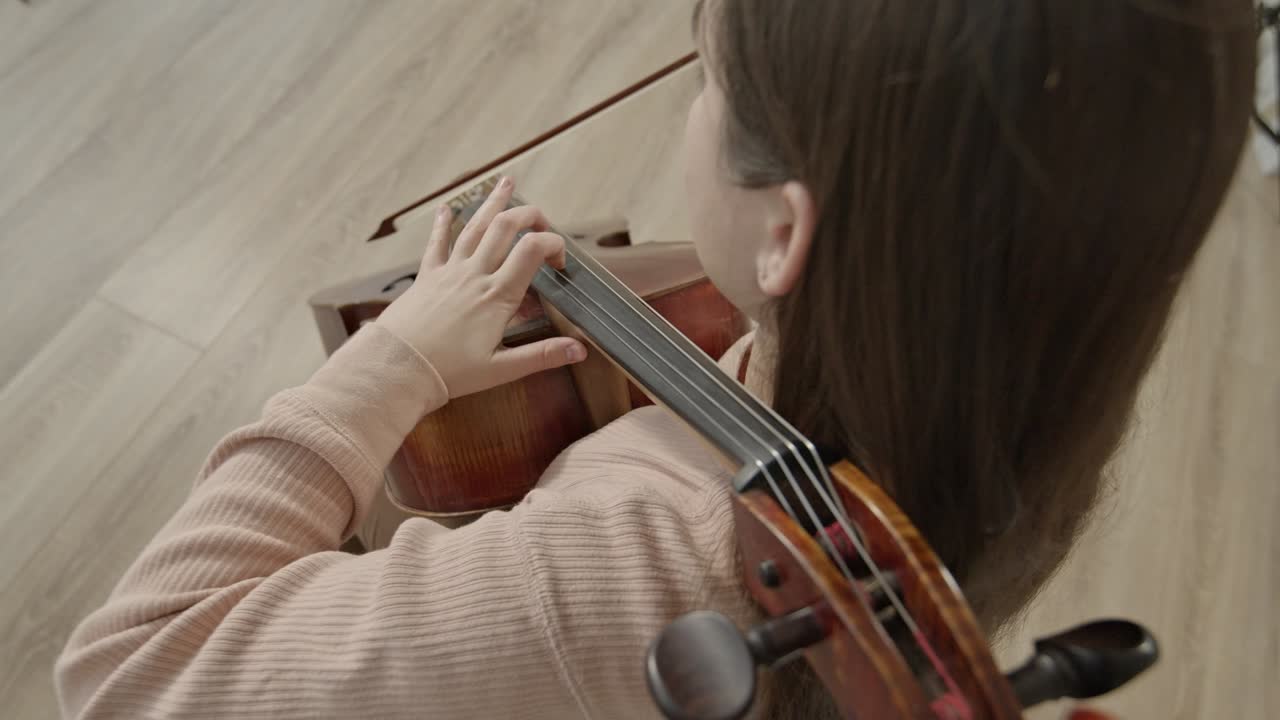 Young woman musician with bow in hands playing cello, top view shot
