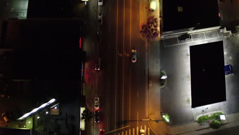 Top-down-view-of-skyscrapers-street-with-vehicles-passing-and-city-lights-at-night