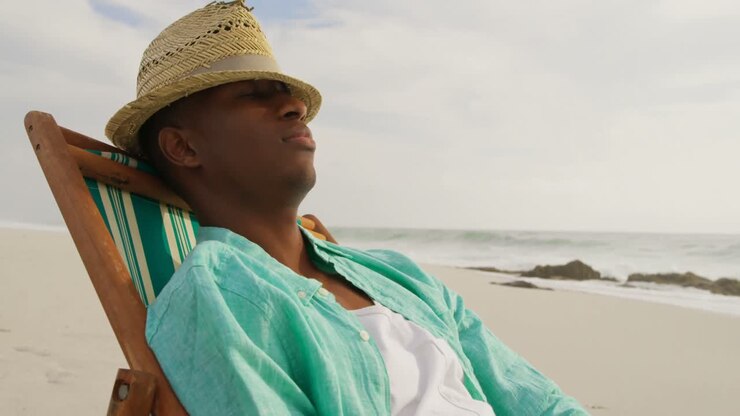 Vista laterale di un uomo afroamericano che dorme su un lettino da sole sulla spiaggia 4K.
