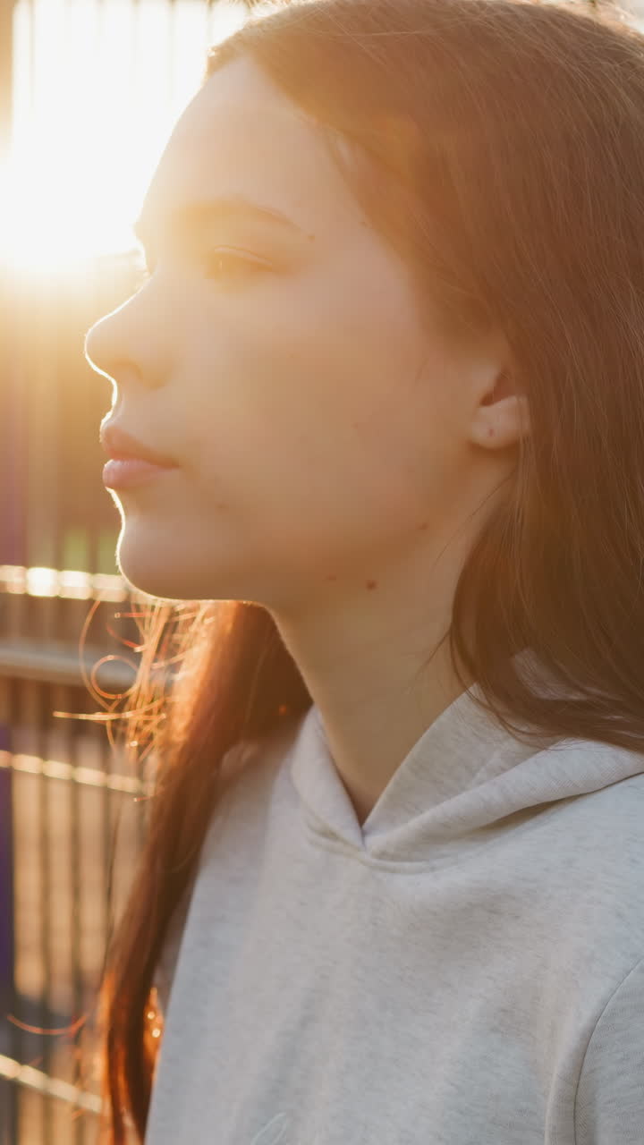 una mujer está de pie junto a la valla de un campo de deportes a la luz del atardecer. una mujer joven se sumerge en pensamientos sobre problemas mientras descansa después del entrenamiento. sensación de vacío