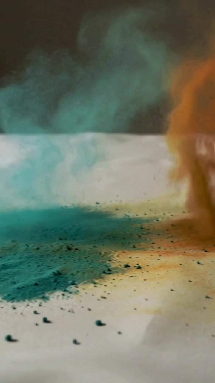 Video verticale: Aria impetuosa che solleva una colonna color verde acqua, che si avvolge e collassa su un tavolo bianco, con l'arancione che sale.