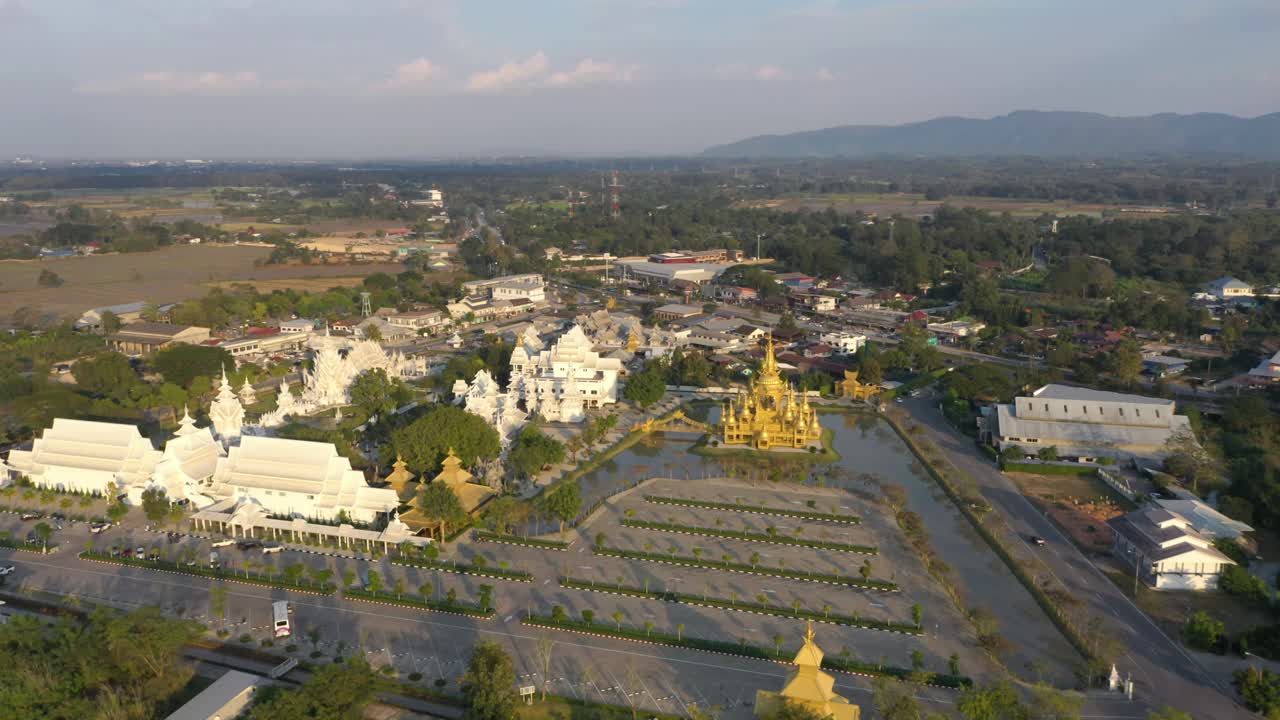 drone aéreo dando vueltas alrededor de wat rong khun el enorme templo budista blanco y templo dorado con montañas y paisaje en chiang rai, tailandia