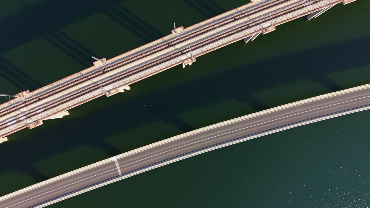 Vista de puente ferroviario sobre el agua con una carretera curva debajo durante el día.