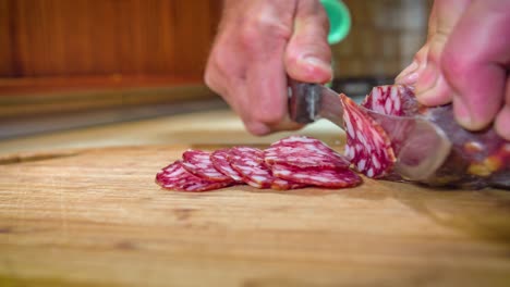 close up shot of a man hands cutting thin slices of salami on a wooden board