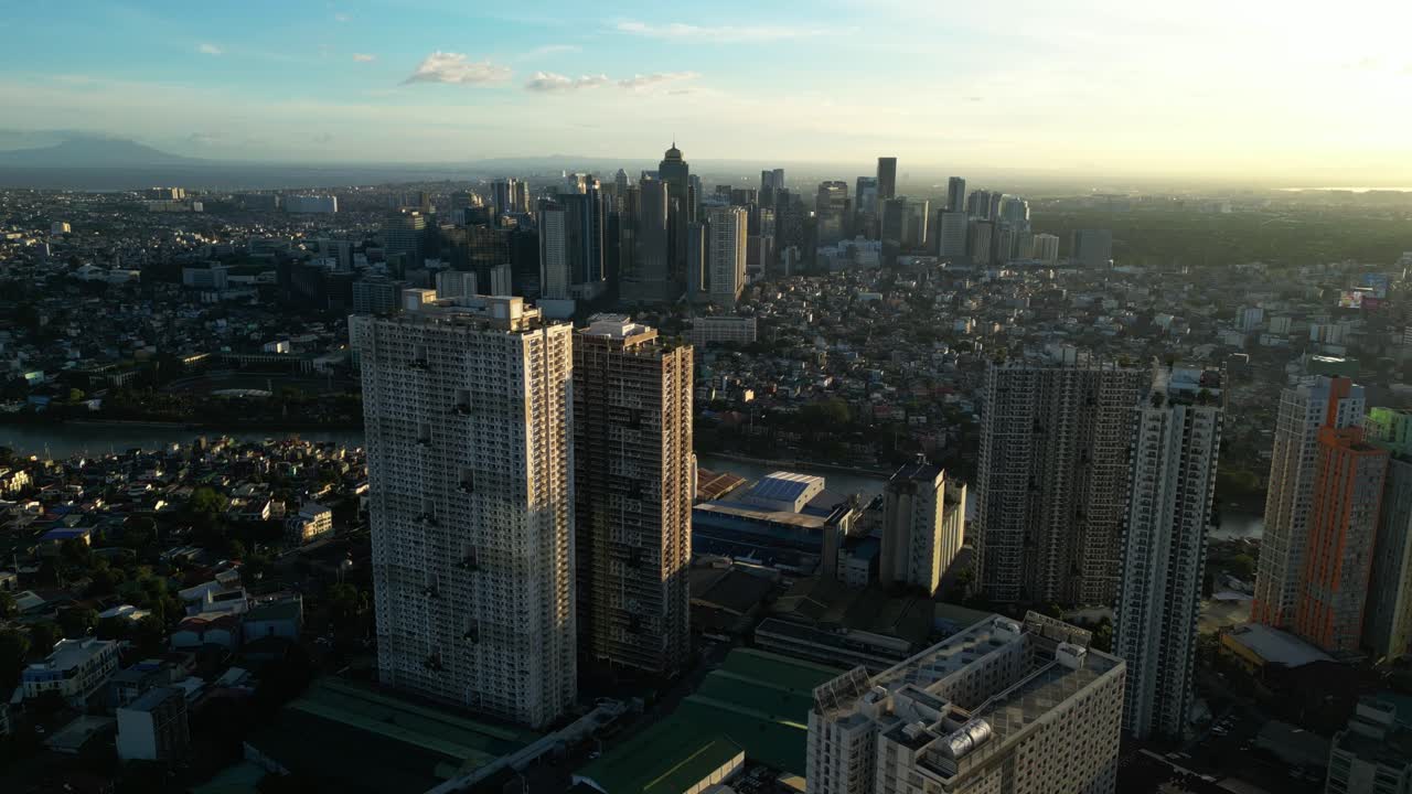 Perspectiva aérea diagonal do skyline de Manila ao pôr do sol, exibindo edifícios em camadas e um horizonte urbano brilhante