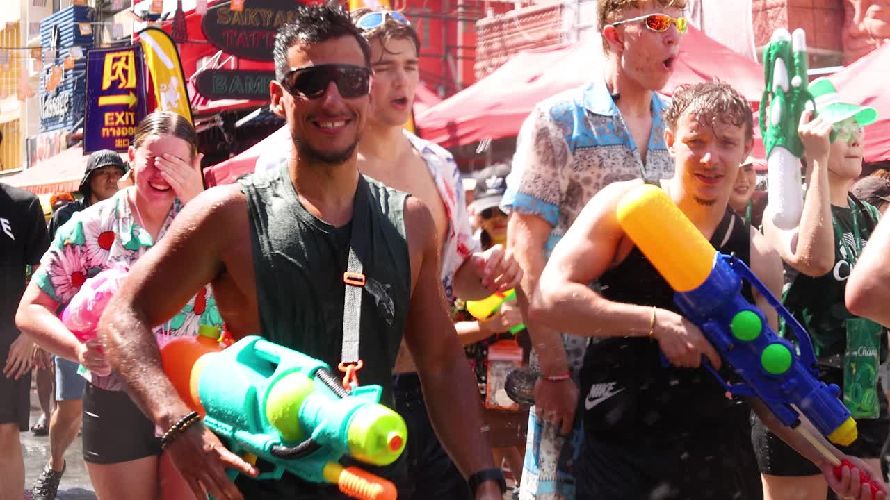Menneskemængder af våde turister fejrer thailandsk nytår med farverige vandpistoler i skarpt sollys