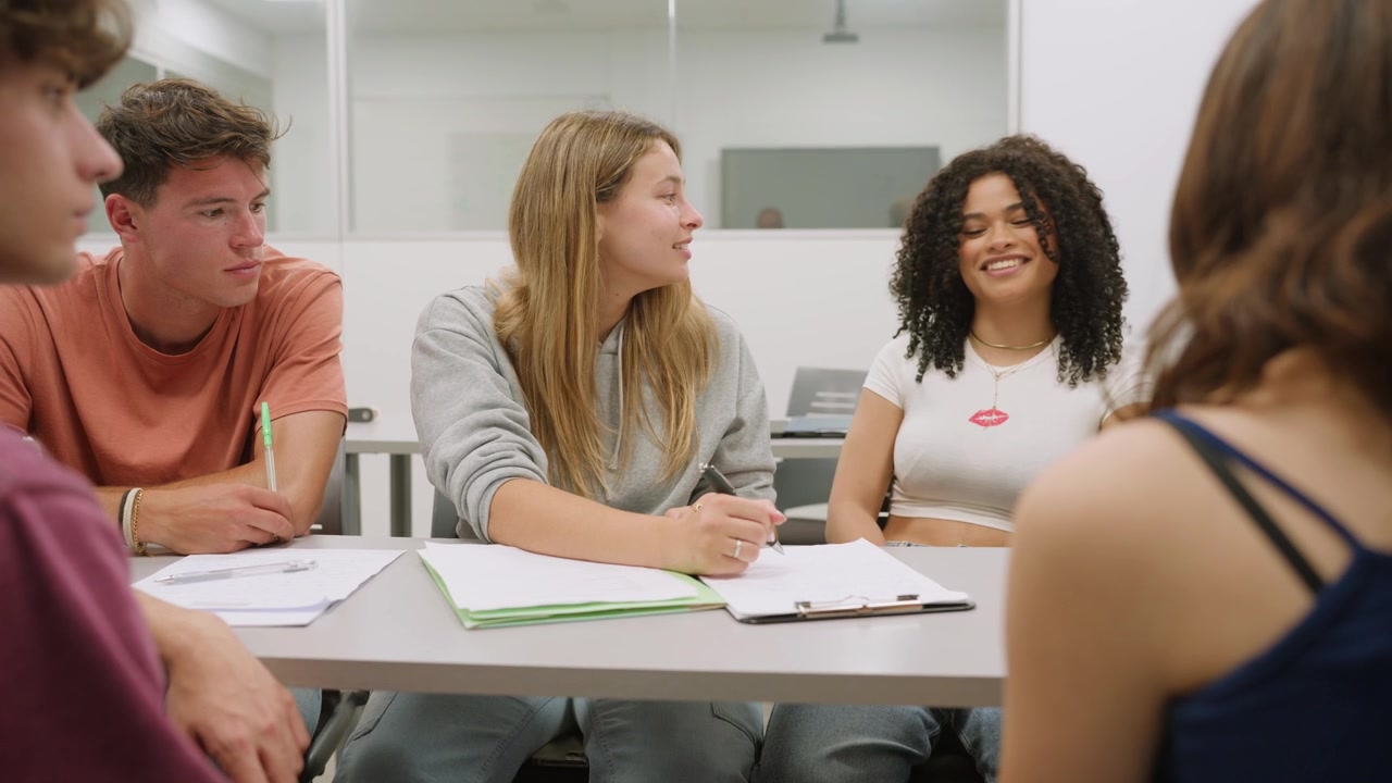 Gruppo di giovani studenti che collaborano e discutono in un'aula moderna.