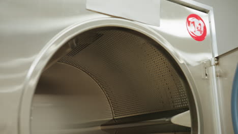 inner view of industrial washer with door open showing stainless steel drum surface and control panel details inside modern laundry facility with bright lighting and reflections on metallic surface
