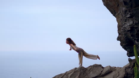 as the sun sets, a young woman practices yoga on a rocky seashore, embodying a healthy lifestyle and the harmony between human and nature, set against the backdrop of the serene blue ocean