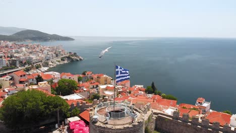 tiro aéreo de retirada de kavala ciudad vieja de grecia y fortaleza, bandera griega ondeando en la parte superior de la torre en el castillo