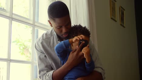 Front-view-of-black-father-and-son-using-smartphone-in-a-comfortable-home-4k