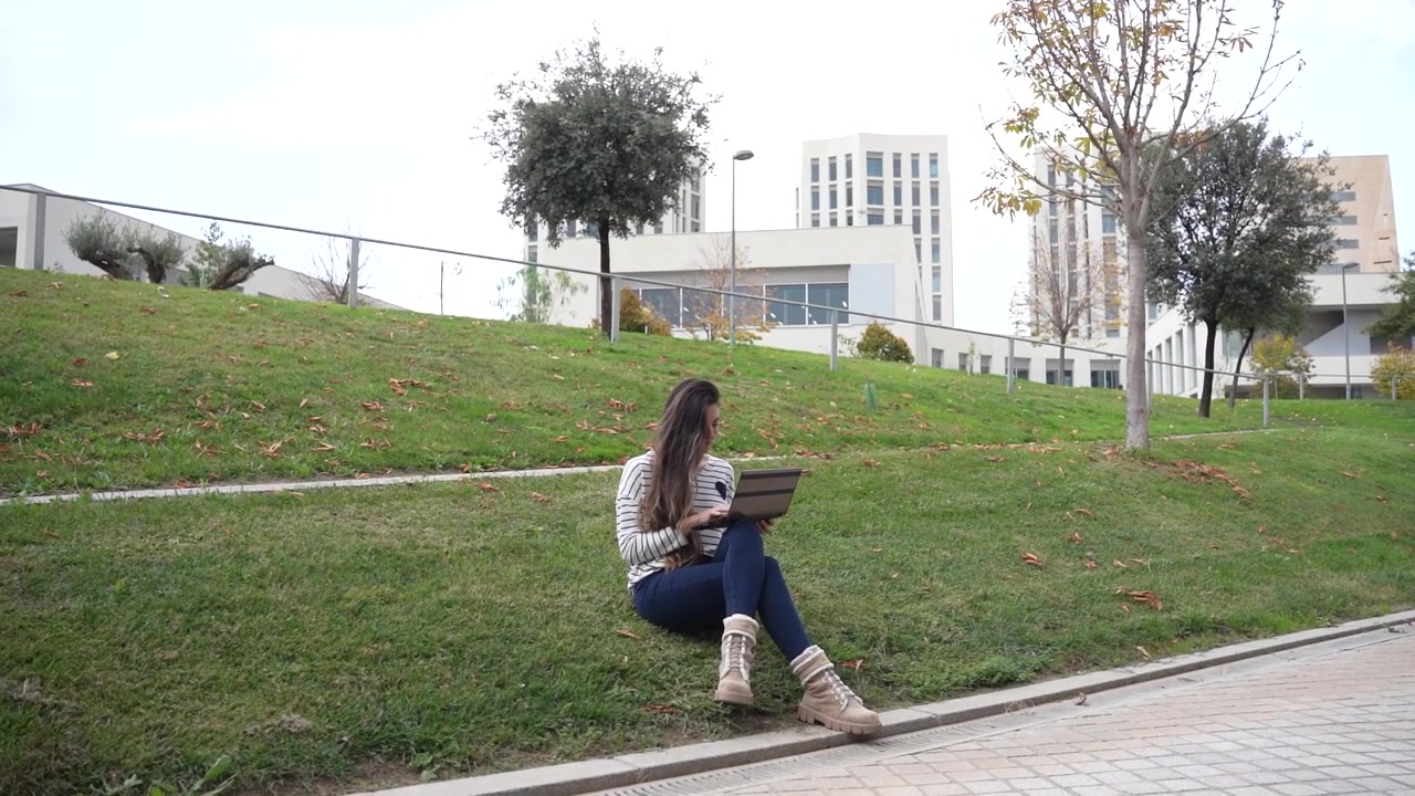 Una giovane donna lavora all'aperto al suo laptop in un ambiente urbano vivace e moderno.