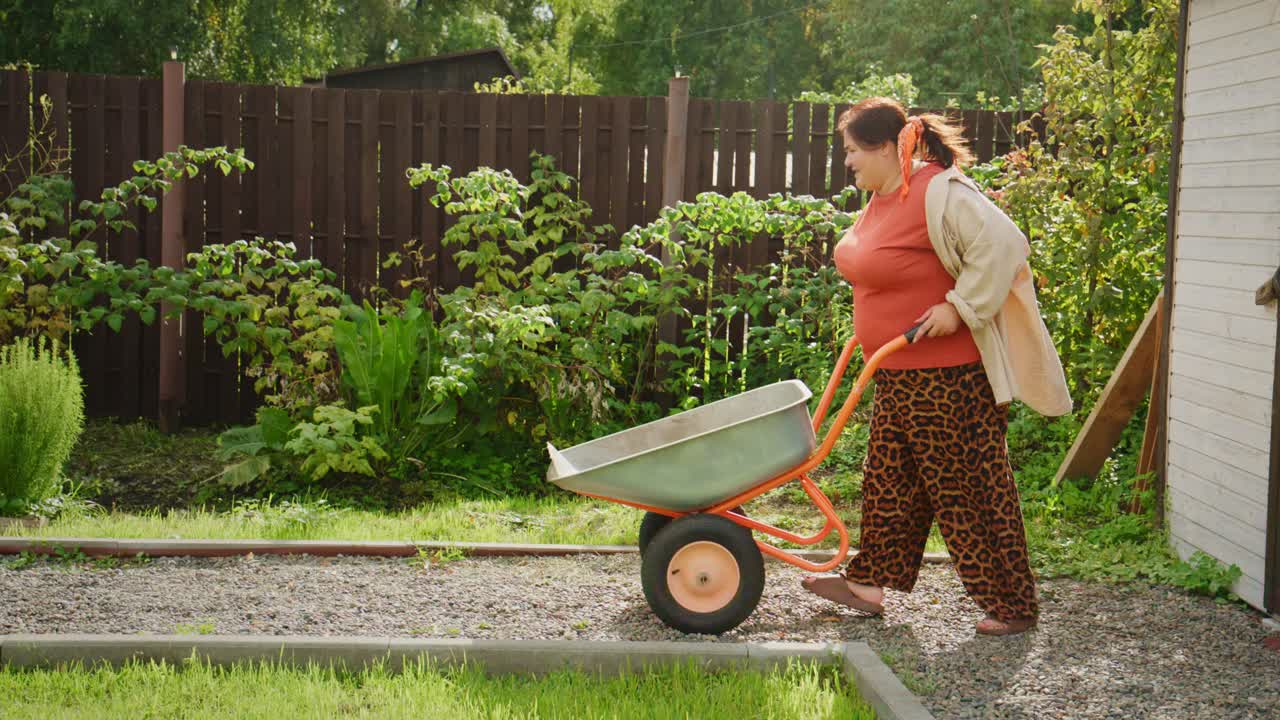 Donna con pantaloni leopardati che spinge una carriola in un giardino: un viaggio nel giardinaggio e nella cura della natura in uno spazio esterno sereno e ricco di vegetazione