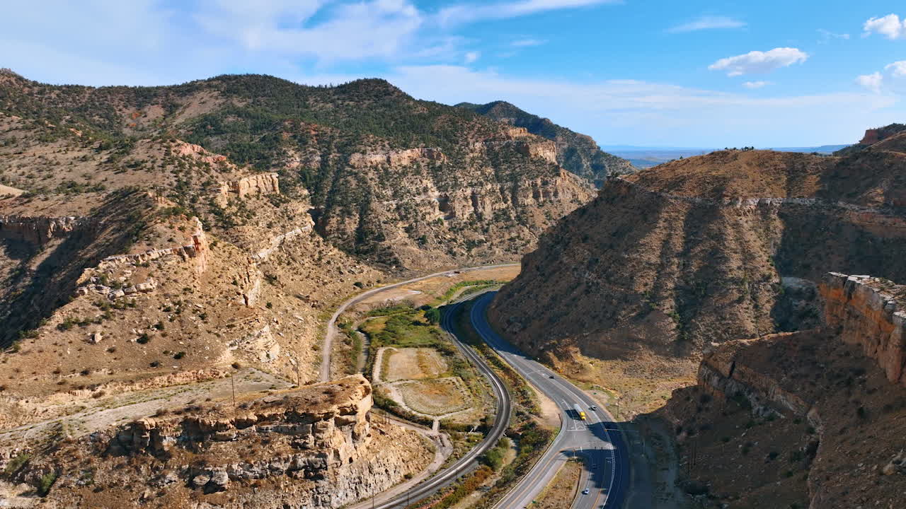 Wide drone view over Price Canyon showing red rock formations, layered cliffs, and a road winding through the valley