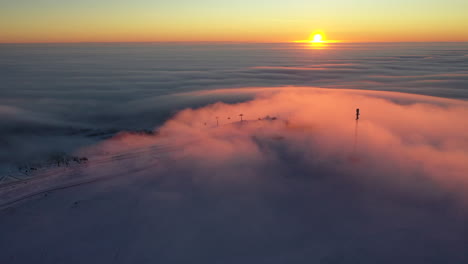 sunrise above clouds turning them into orange at the top of a ski resort