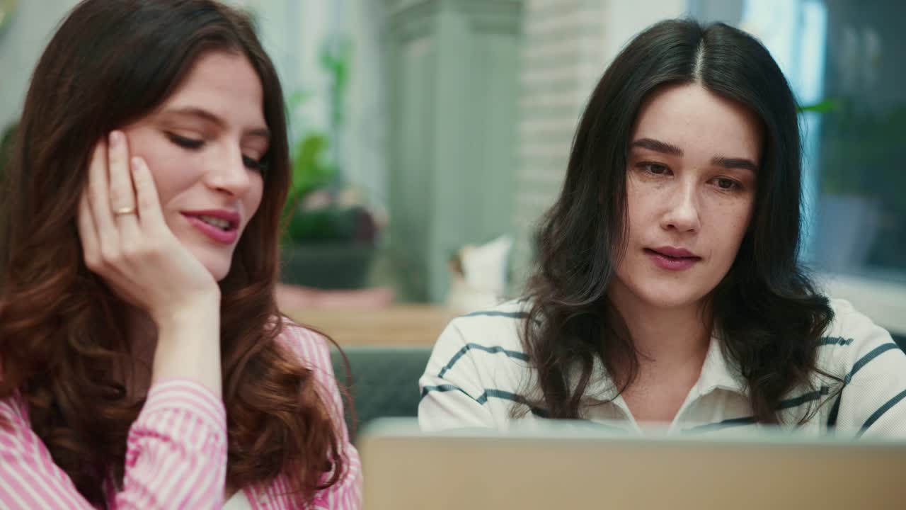 Two Young Women Collaborating and Smiling While Using a Laptop