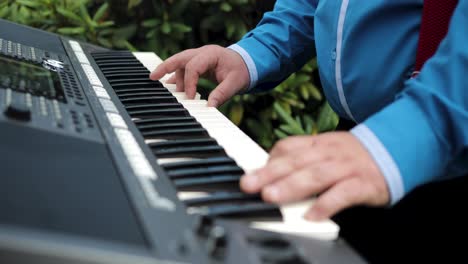 medium shot of a man with blue shirt playing a synthesizer keyboard in the garden