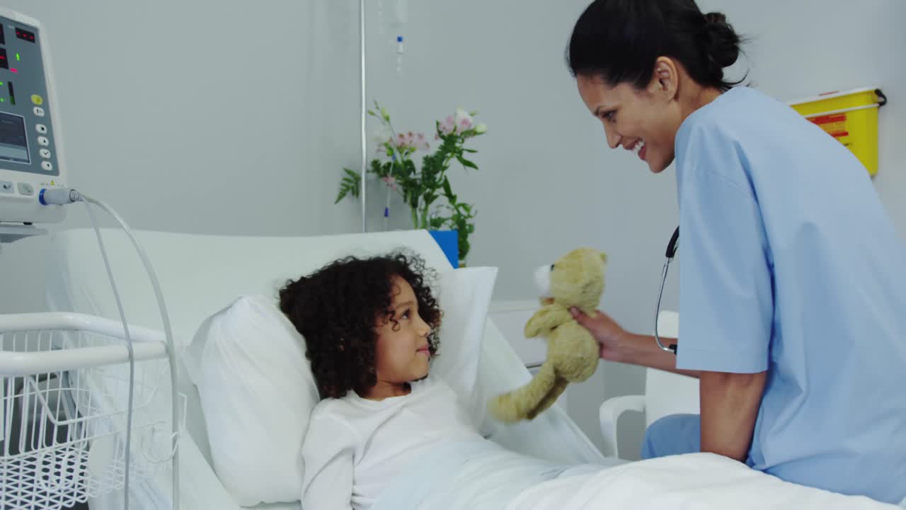 Side view of African american female doctor giving teddy bear to child patient in the ward 4k