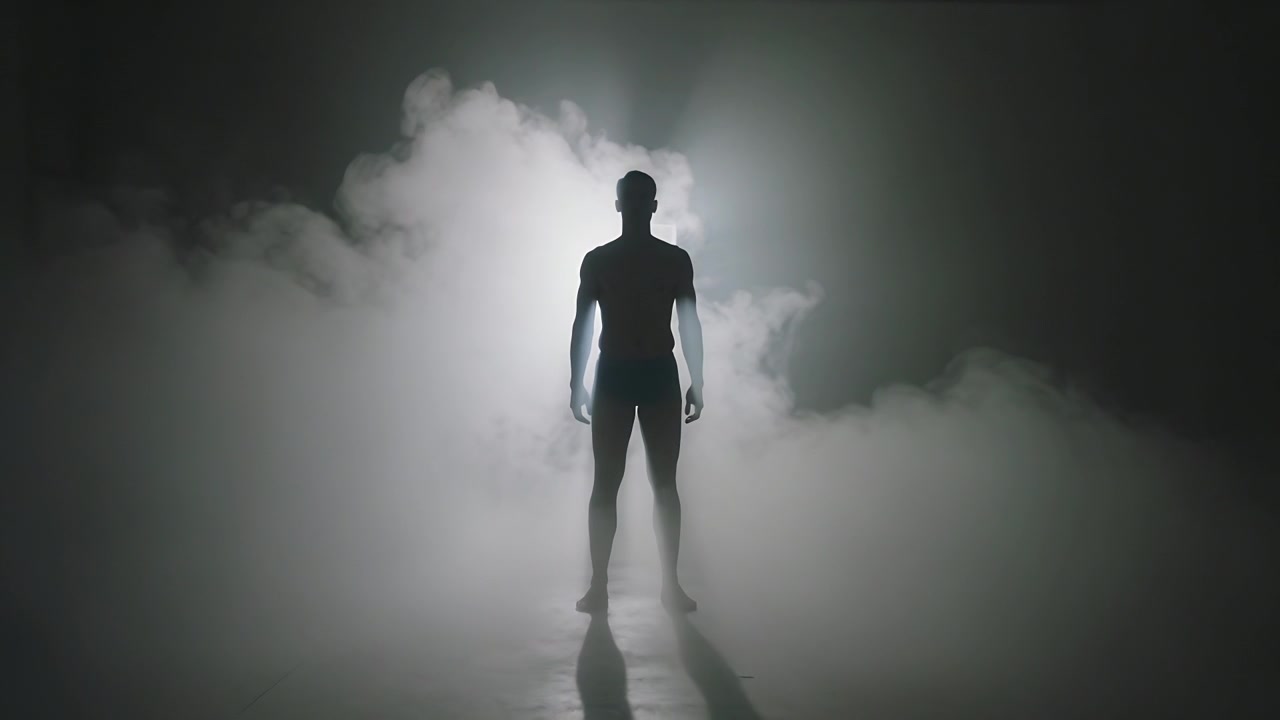 Hombre en traje oscuro revelándose de pie en el escenario, con luz de fondo ascendente para una revelación visual y niebla rodando.