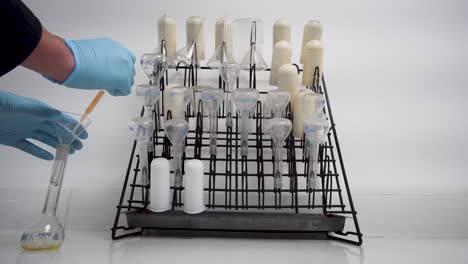el trabajador de laboratorio caucásico deja caer un químico líquido en un matraz volumétrico, utensilios en el estante