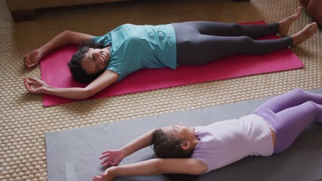 madre e hija de raza mixta practicando yoga en la sala de estar