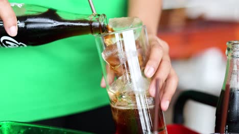 person pouring cola into a glass with ice