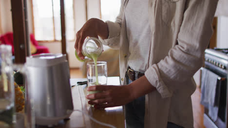 Midsection-of-mixed-race-woman-preparing-health-drink-standing-in-cottage-kitchen-smiling