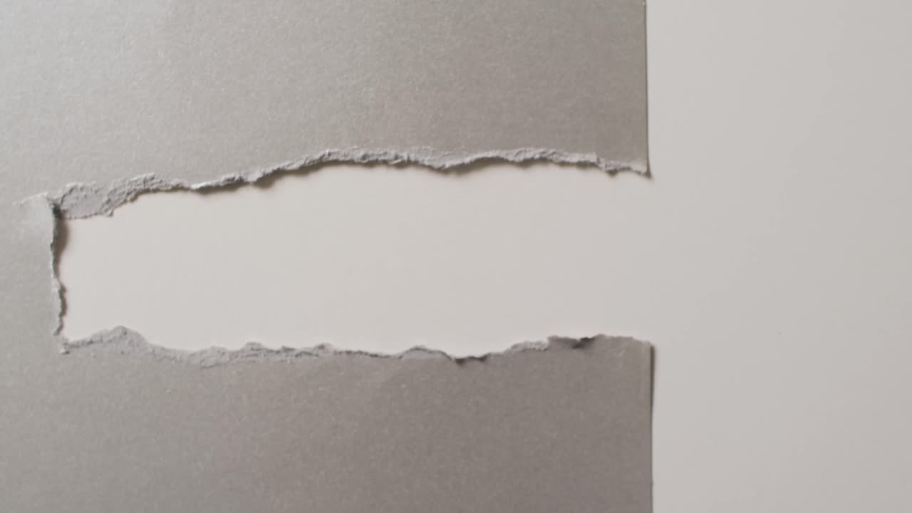 Video of close up of torn grey paper on white background